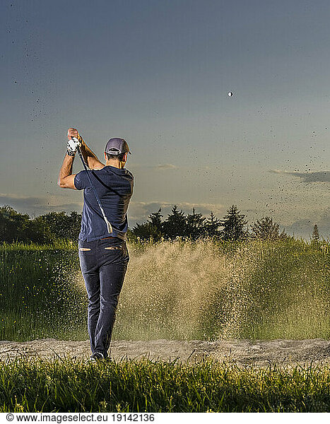 Man hitting golf ball on grass at dusk