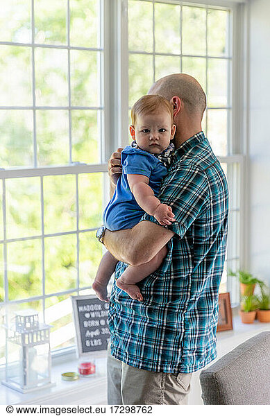 Man holding baby boy near window.