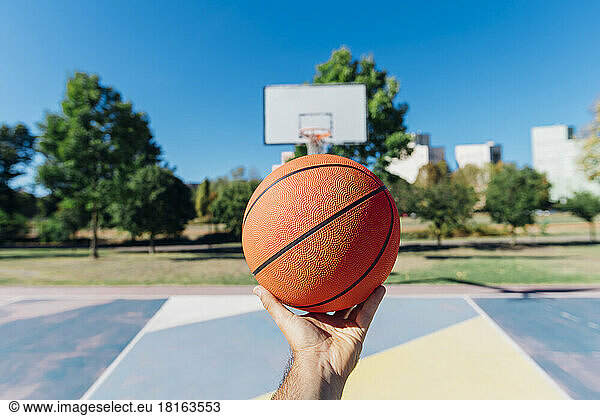 Man holding basketball at court on sunny day