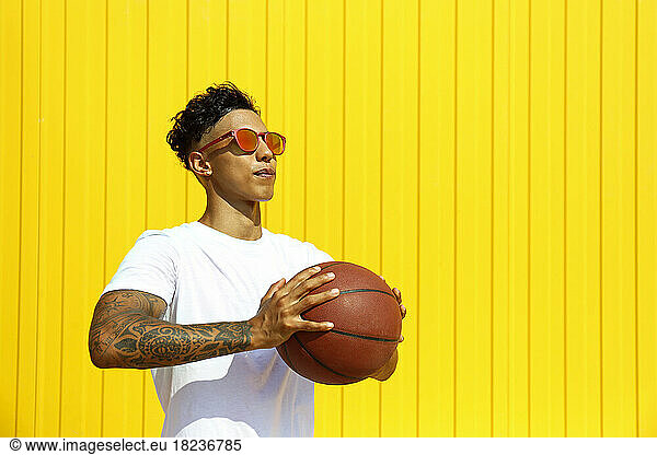 Man holding basketball in front of yellow wall
