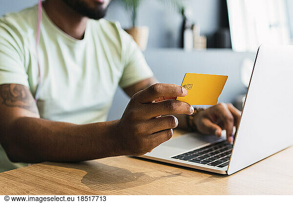 Man holding credit card by laptop in desk at home