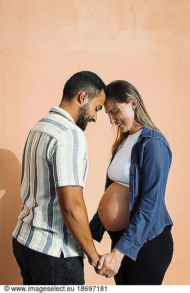 Man holding hands and standing with pregnant woman in front of wall
