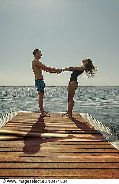 Man holding hands of woman standing on pier at sunny day