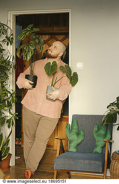 Man holding houseplants and leaning on doorway at home
