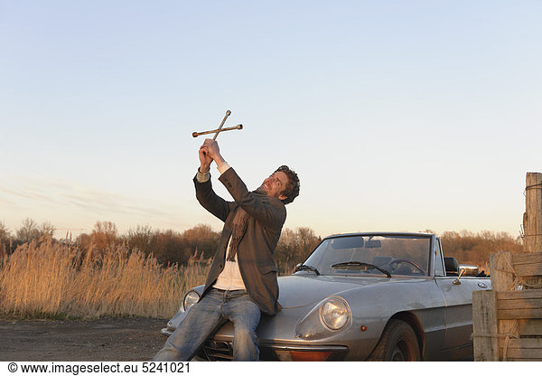 Man holding lug wrench as cross near classic cabriolet car