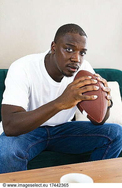 Man holding rugby ball while sitting on sofa at home