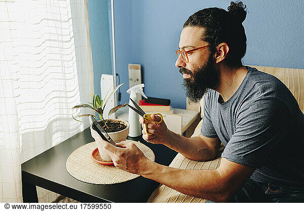 Man holding scissors using mobile phone sitting on sofa at home