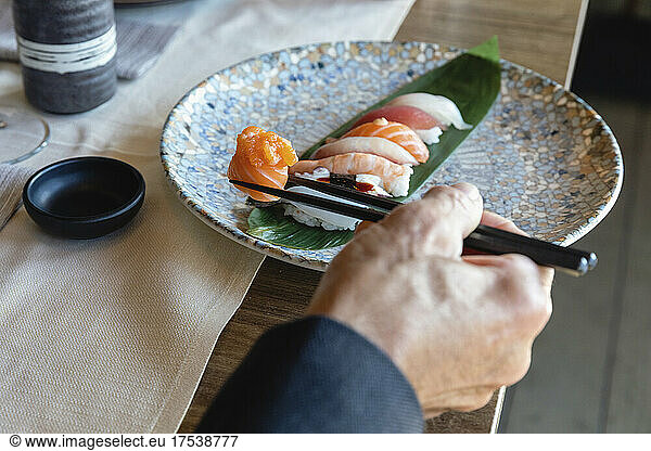 Man holding sushi on chopsticks at restaurant