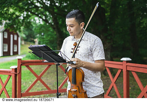 Man holding violin reading sheet music at park