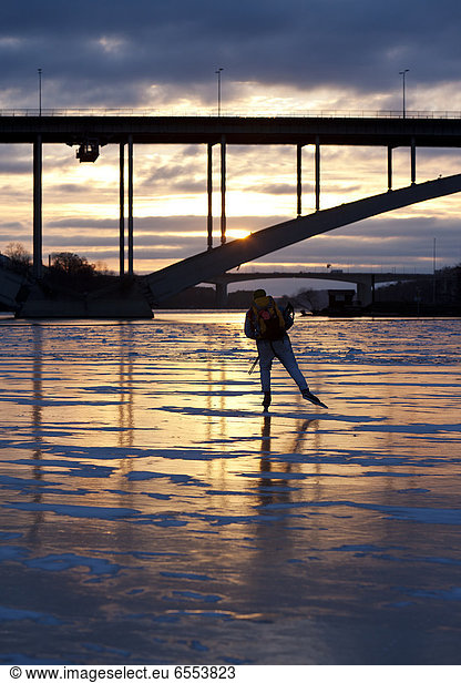 Man ice skating on frozen river at sunset