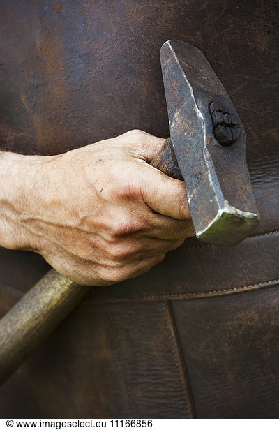 Man in a leather apron holding a hammer.