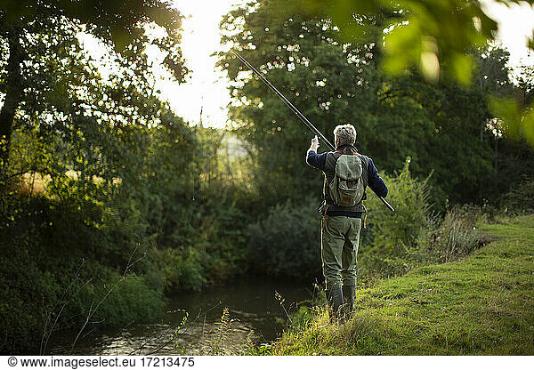 Man in backpack fly fishing at riverbank