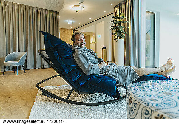 Man in bathrobe relaxing on rocking chair in hotel room