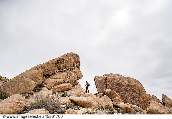 Man in between strange rock formation in desert under gray sky
