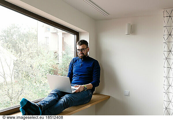 man in blue sweater and jeans is working alone at home with laptop