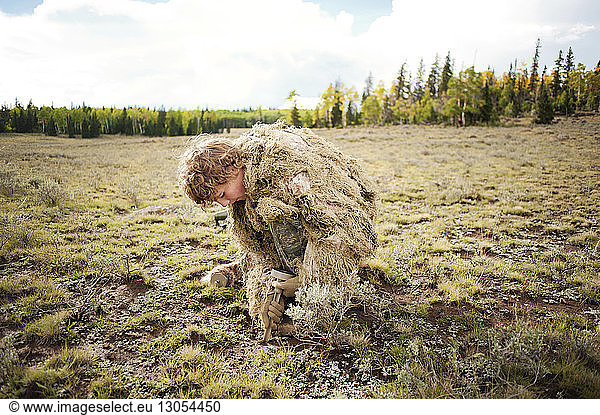 Man in camouflage clothing digging on field