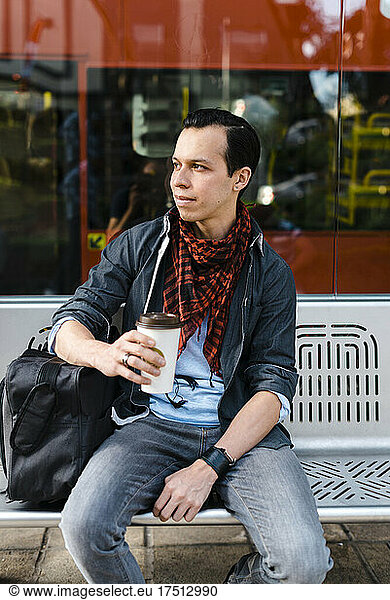 Man in casuals having coffee while waiting for bus at station