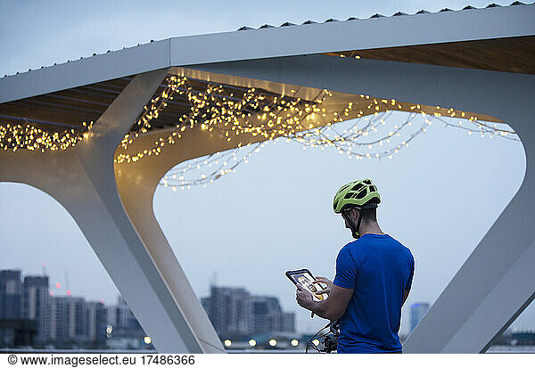 Man in helmet using digital tablet below illuminated bridge  London