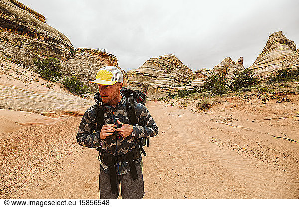 man in hiking hat and camo jacket buckles his chest strap in desert