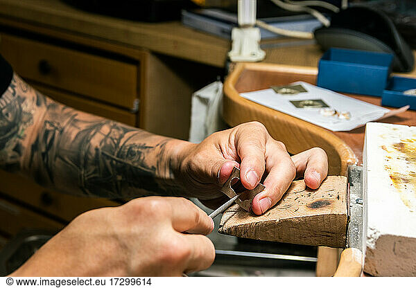 Man in jewelry workshop filing a piece of silver.