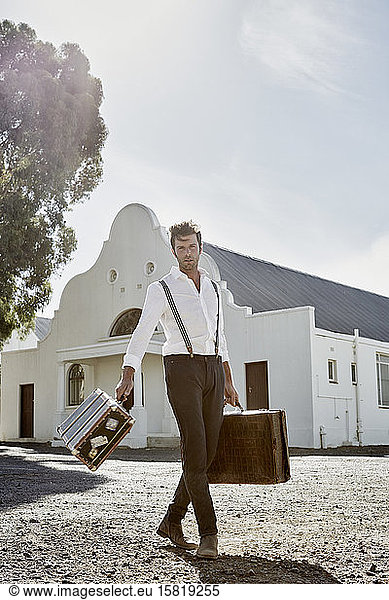 Man in old-fashioned clothes with suitcases walking in the countryside