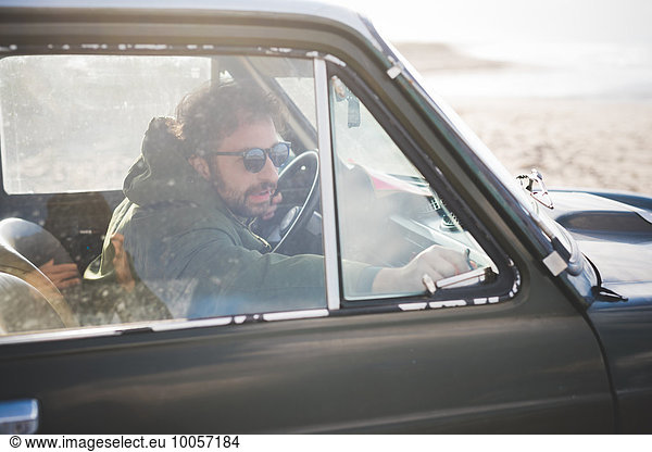 Man in parked vintage car lat beach fastening window