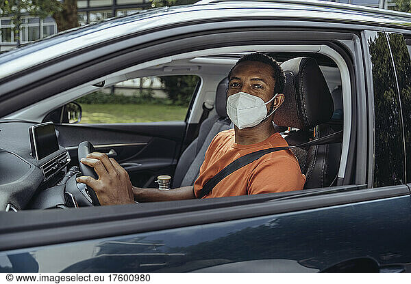 Man in protective face mask driving car in COVID-19 outbreak