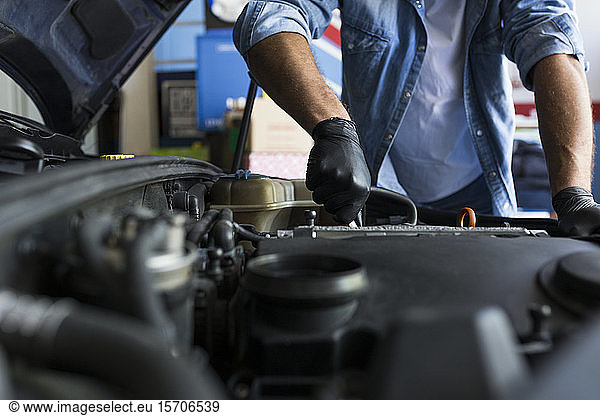 Man in shirt and gloves working in car repair service and fixing car engine