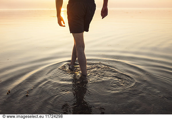 Man in shorts wading in sea at sunset