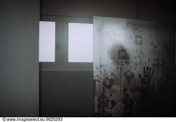 Man in shower with hand prints on glass pane