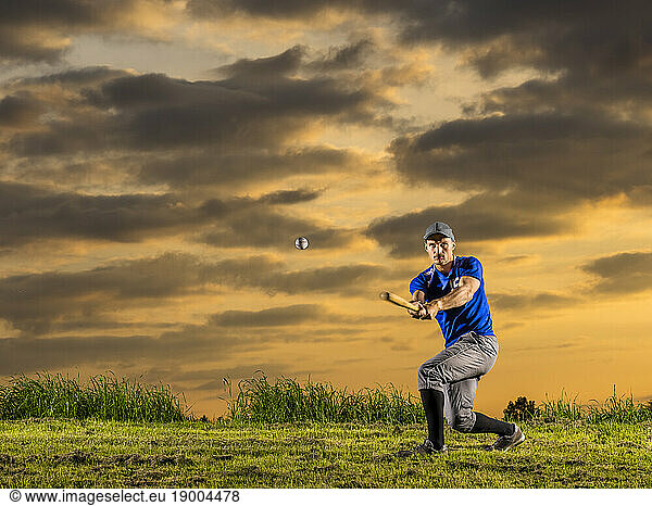 Man in sports clothing hitting baseball with bat in dusk
