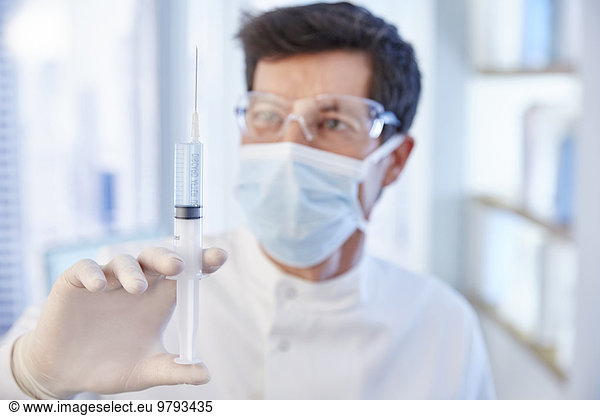 Man in surgical mask and labcoat holding syringe with fluid