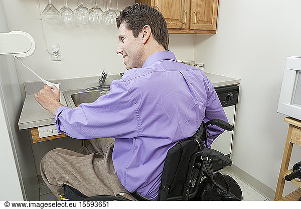 Man in wheelchair with spinal cord injury using a paper towel rack in an accessible kitchen