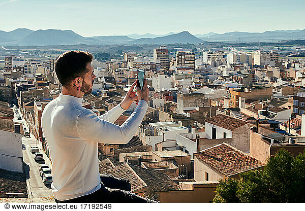 Man is sitting on a rooftop taking pictures with his phone
