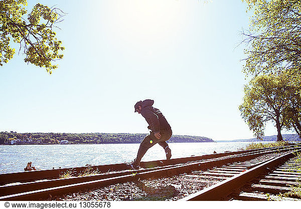 Man jumping on railroad tracks by river against clear sky