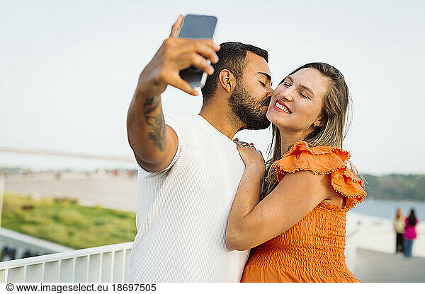 Man kissing and taking selfie with pregnant woman