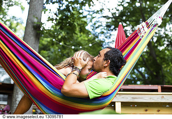 Man kissing daughter on forehead while relaxing in hammock at backyard