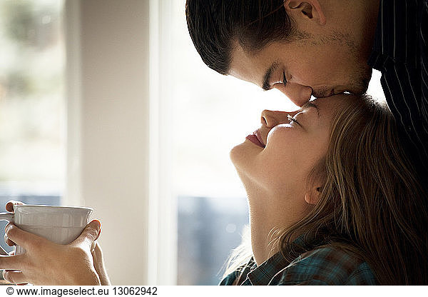 Man kissing girlfriend on forehead at home