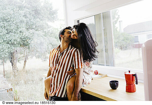 Man kissing girlfriend sitting on kitchen counter at home
