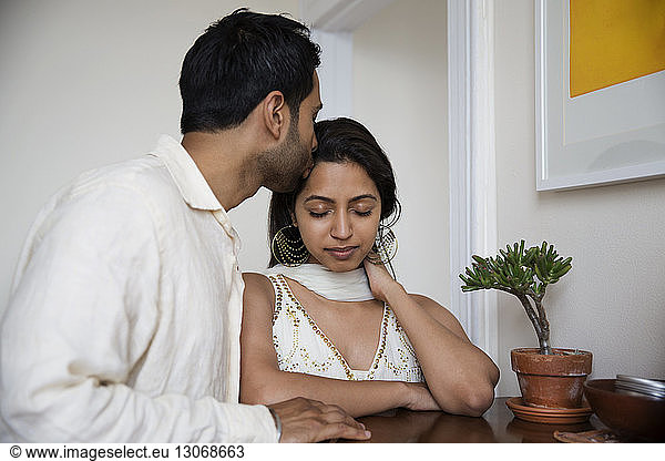 Man kissing woman on forehead while standing by table at home