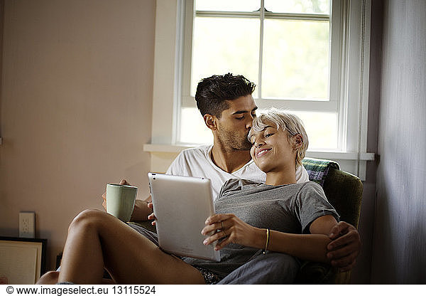 Man kissing woman using tablet computer at home