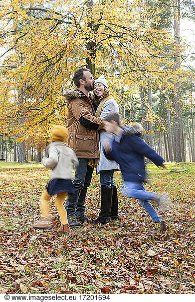Man kissing woman while standing with children playing around in forest