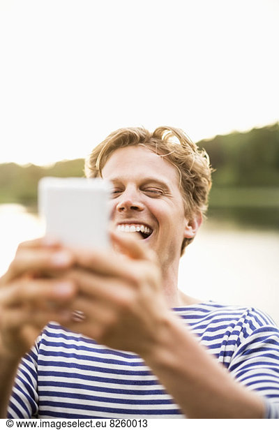 Man laughing while reading text message on mobile phone outdoors
