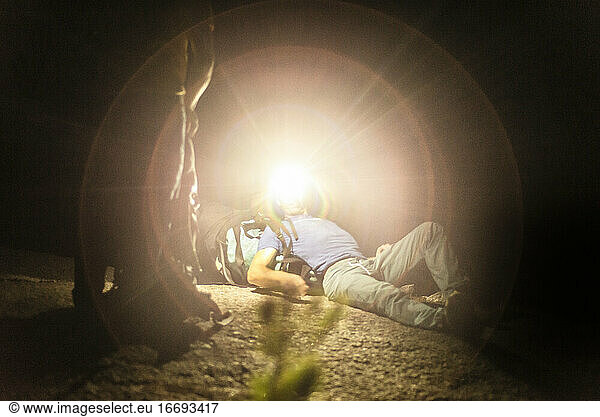 Man laying down with big backpack looking up with headlamp at night