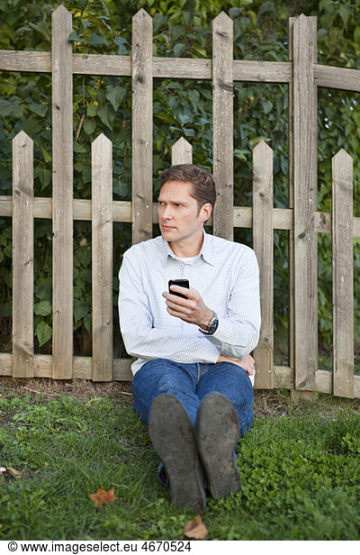 Man leaning against fence with cellphone in his hand