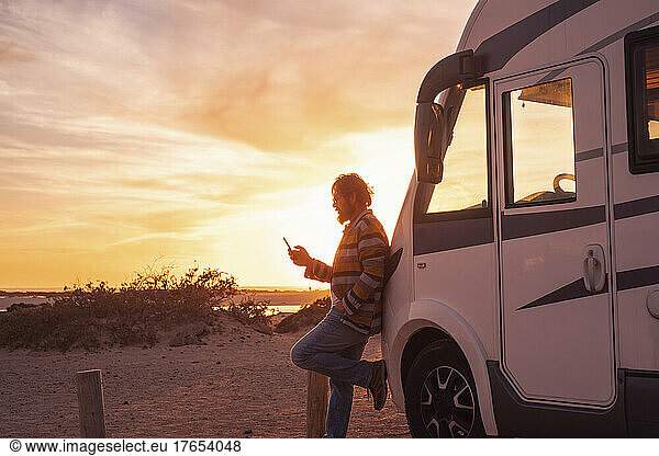 Man leaning on camper van and using smart phone