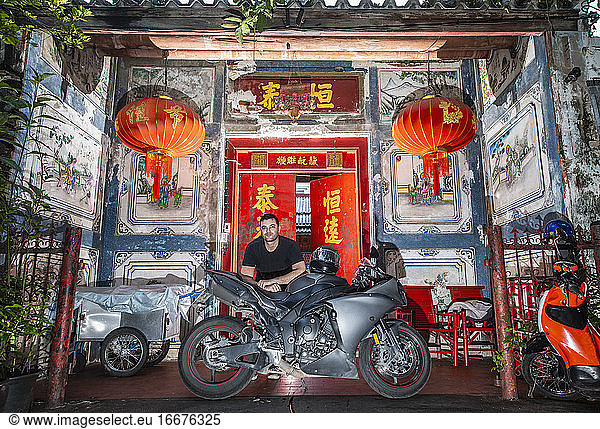 man leaning on his motorcycle in front of Chinese house in Bangkok