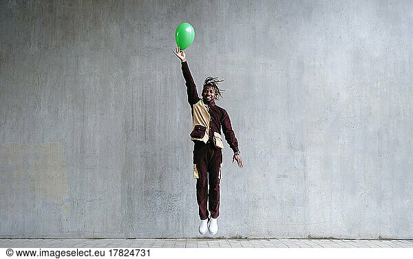 Man levitating with hand raised holding balloon in front of concrete wall