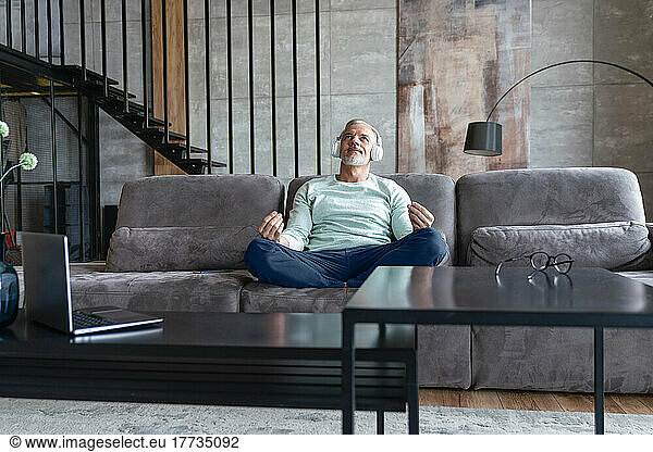 Man listening music through wireless headphones mediating on sofa at home