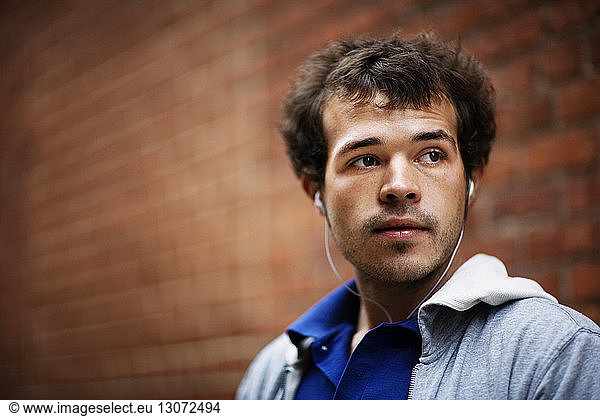 Man listening music while standing against brick wall
